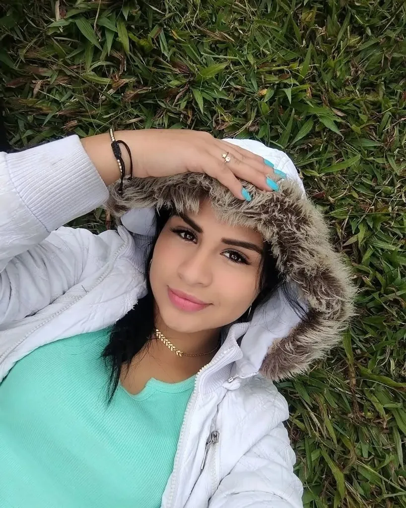 Dr. María Fernanda Terán lying on the grass, wearing a white hooded jacket and a turquoise shirt.
