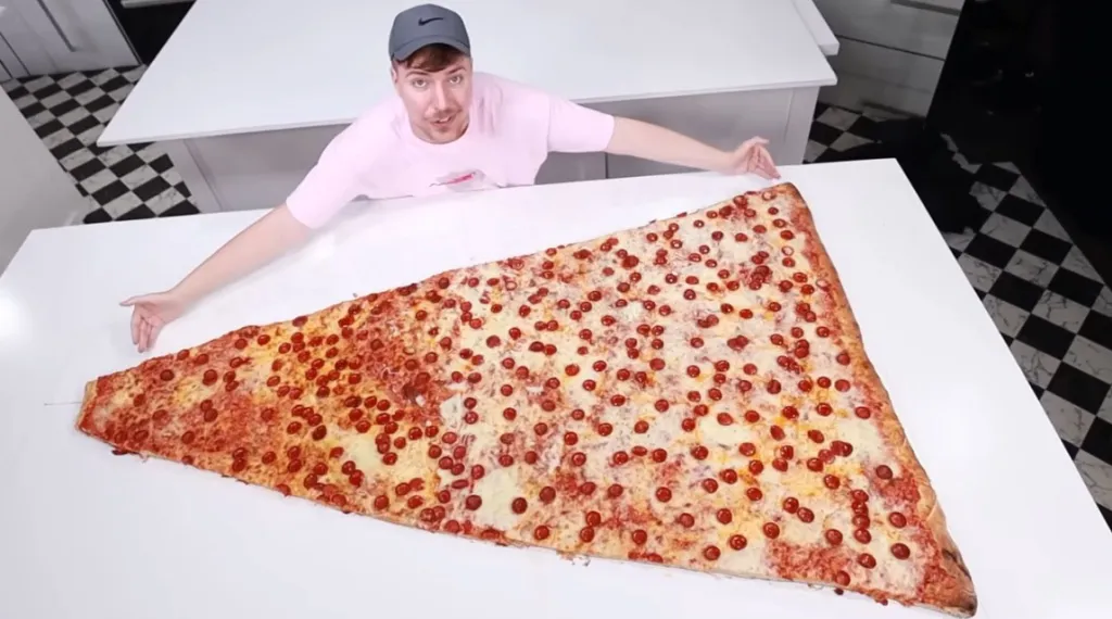 Mr. Beast sitting behind a very large slice of pepperoni pizza.
