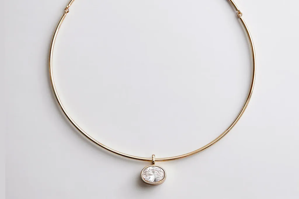 A gold choker necklace with an oval-cut diamond in a bezel setting.