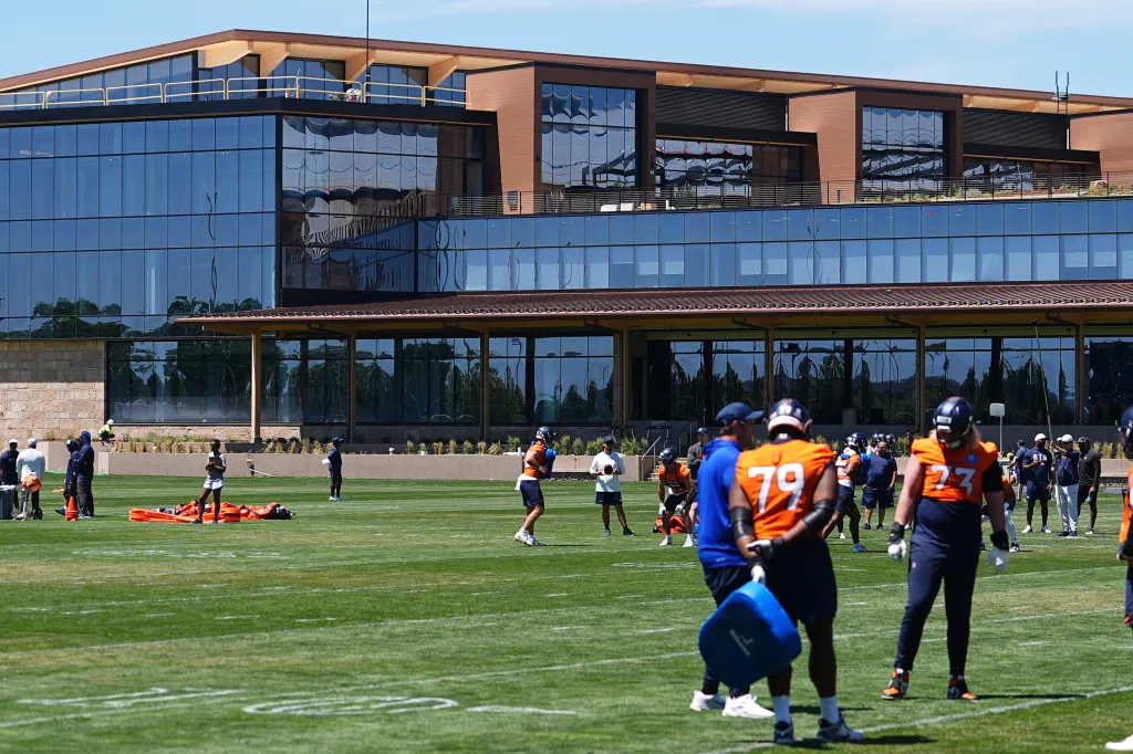 Denver Broncos players practicing football drills in front of the team's new headquarters.