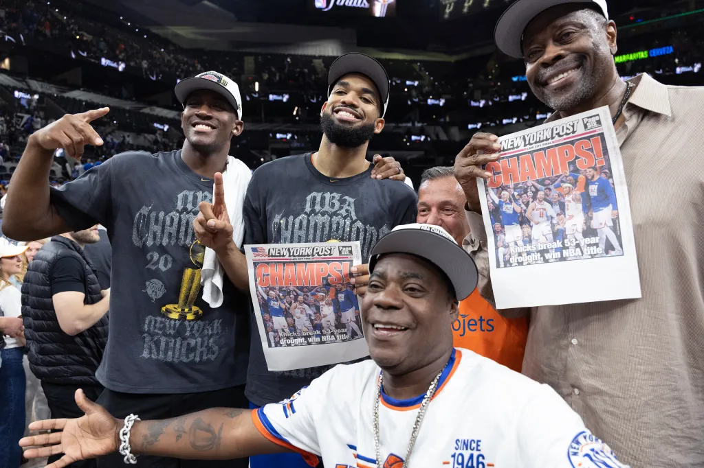 Karl-Anthony Towns (c.) and Patrick Ewing (r.) hold up the New York Post cover after winning the NBA championship on June 13, 2026.