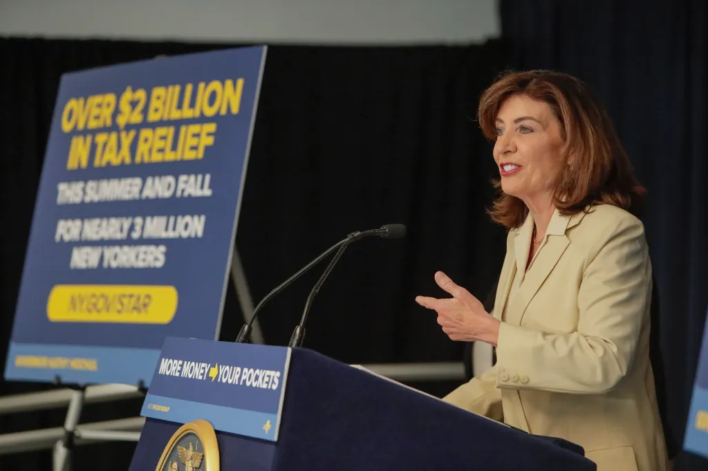 Governor Kathy Hochul speaking at a podium about New York's School Tax Relief (STAR) program, with a sign stating "Over $2 Billion in Tax Relief This Summer and Fall for Nearly 3 Million New Yorkers".