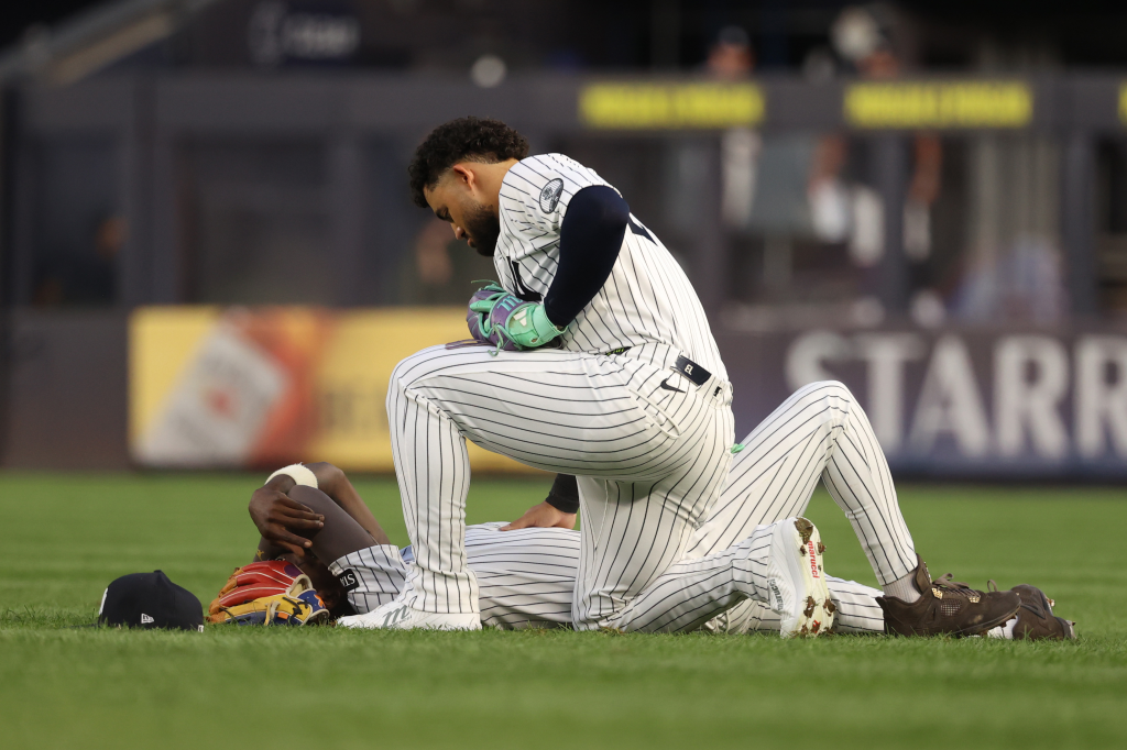 New York Yankees' Jasson Domínguez kneels to check on teammate Jazz Chisholm Jr. who is lying on the grass after a collision.