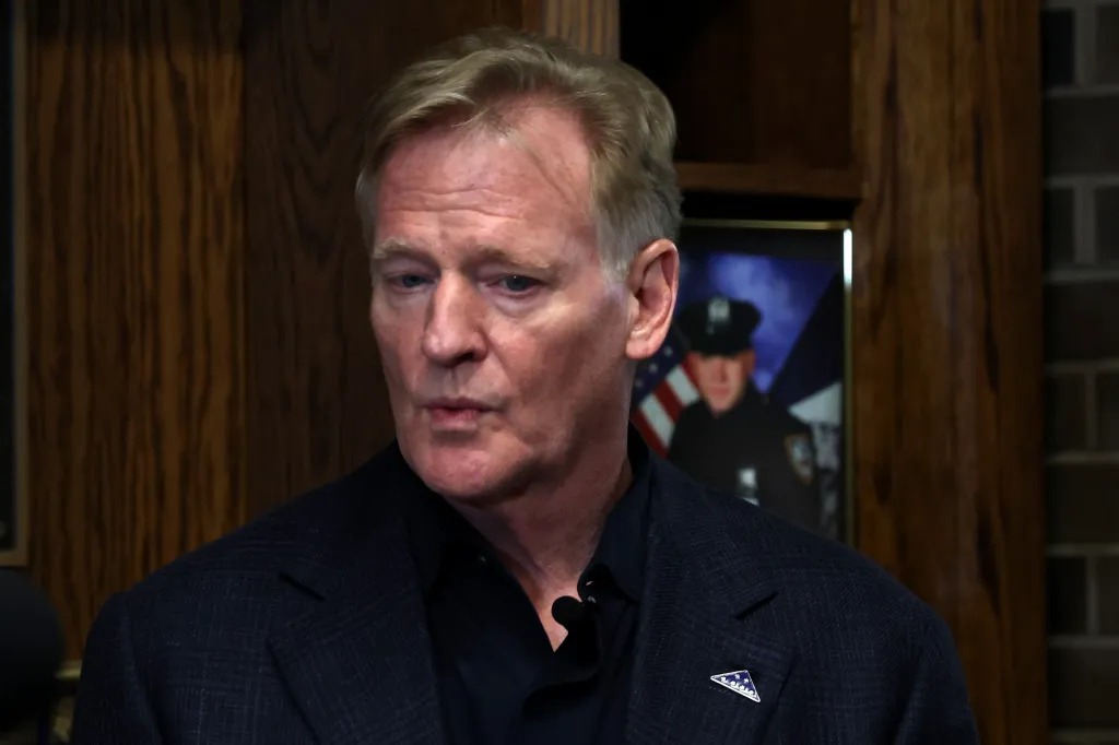NFL Commissioner Roger Goodell wearing a blue suit and a small microphone pinned to his shirt.