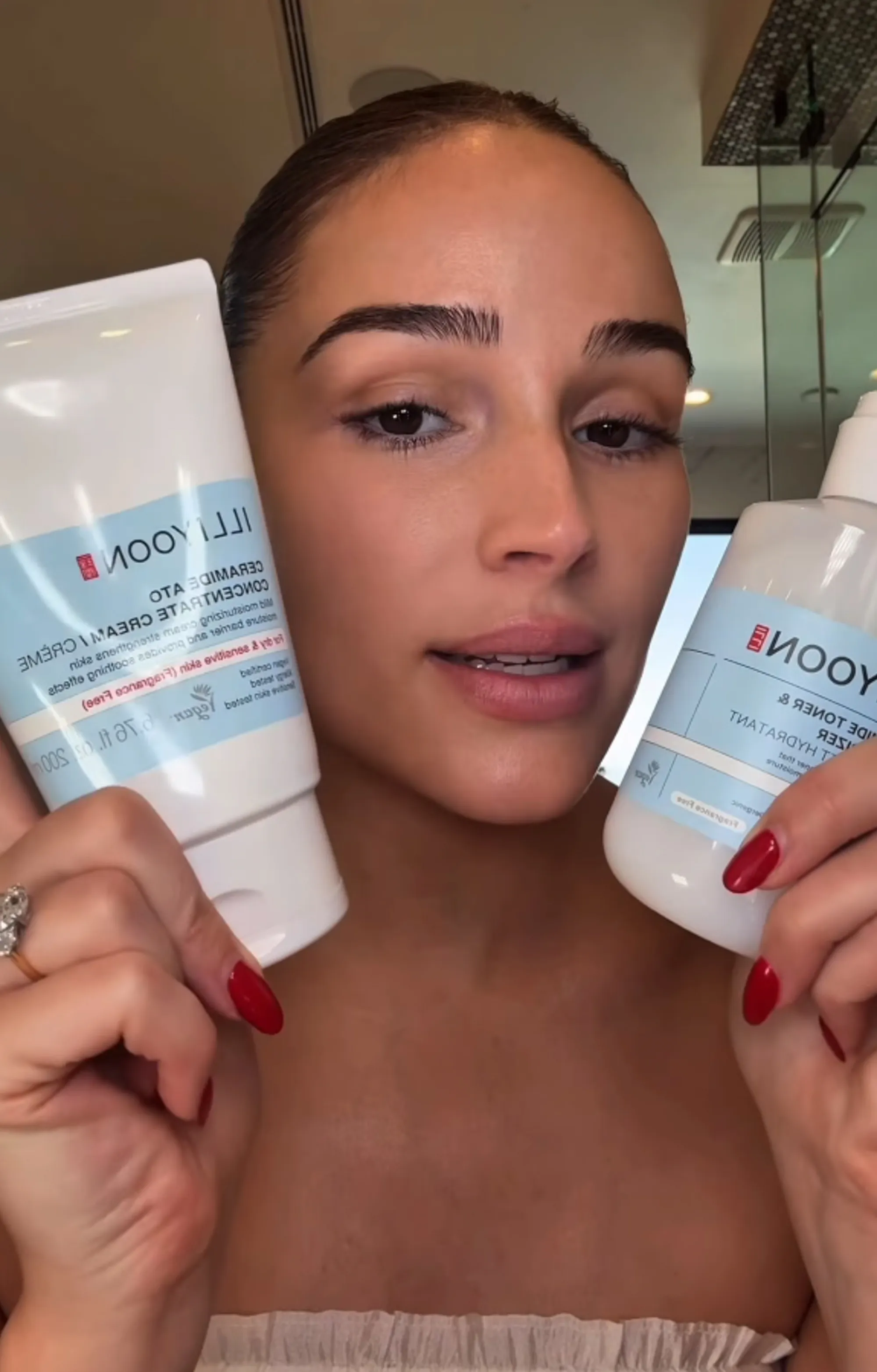 Olivia Culpo holds up a large tube of Illiyoon Ceramide Ato Concentrate Cream and a bottle of Illiyoon Ceramide Ato 6.0 Side Toner & Hydrator.