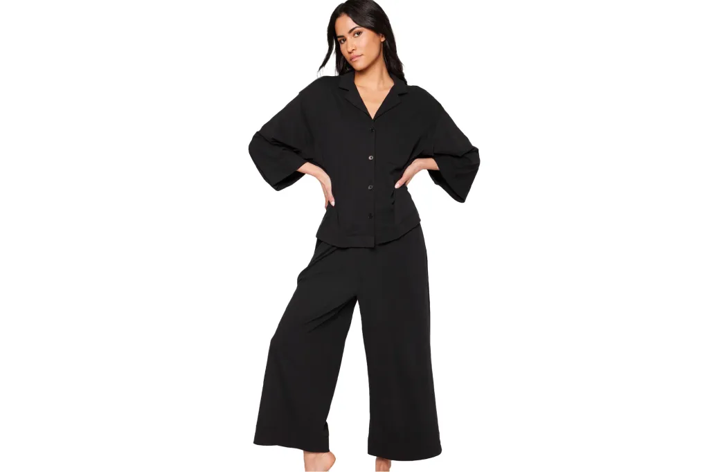 Woman with dark hair posing in a black button-up top and matching wide-leg pants.
