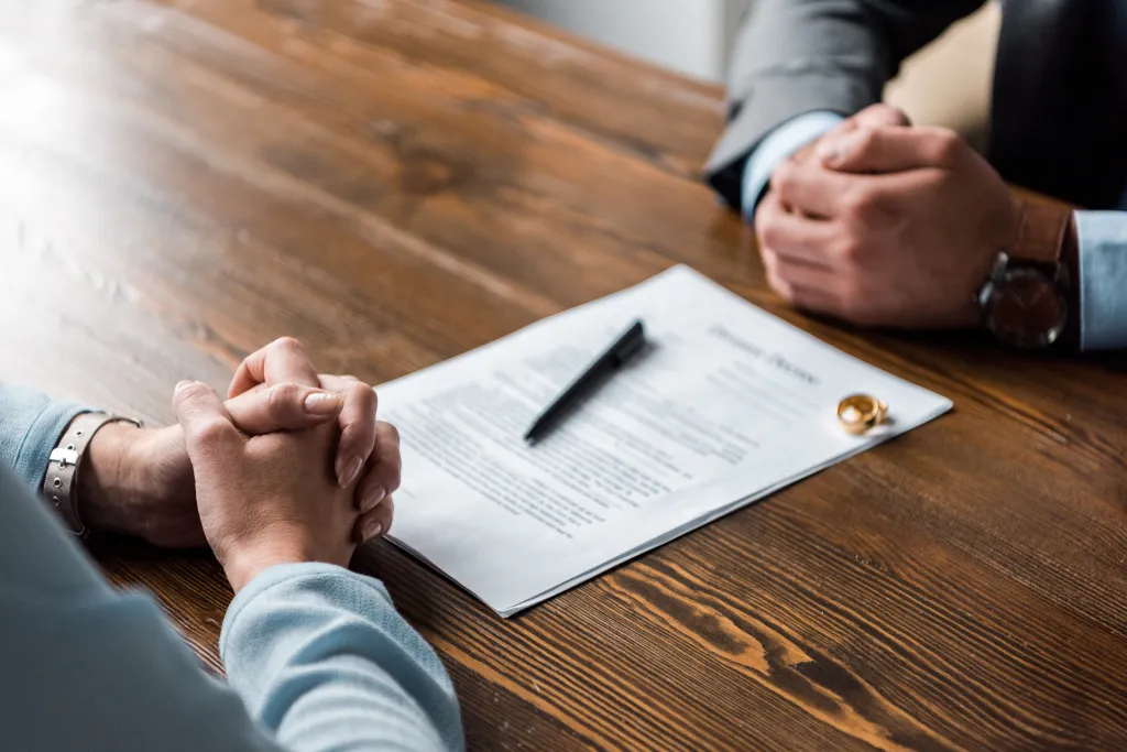 Hands of a lawyer and client at a table with divorce papers and wedding rings.