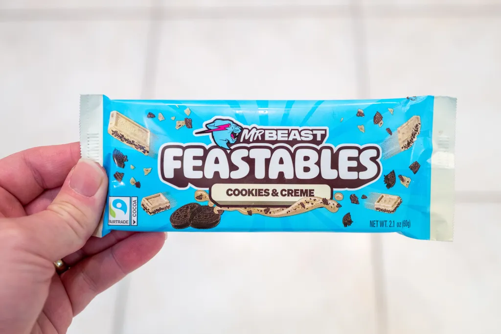 A hand holding a blue Mr. Beast Feastables Cookies & Creme chocolate bar.