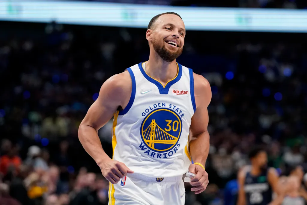 Stephen Curry smiling and wearing his Golden State Warriors jersey during a basketball game.