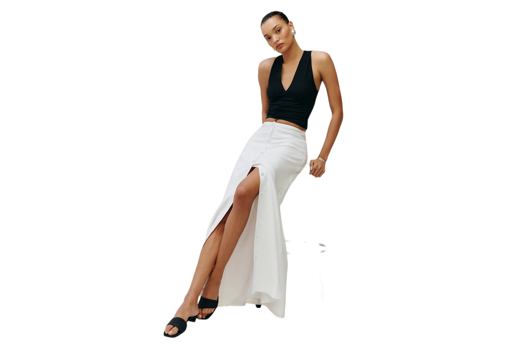 A woman wearing a black sleeveless top, a white long skirt with a slit, and black heeled sandals.