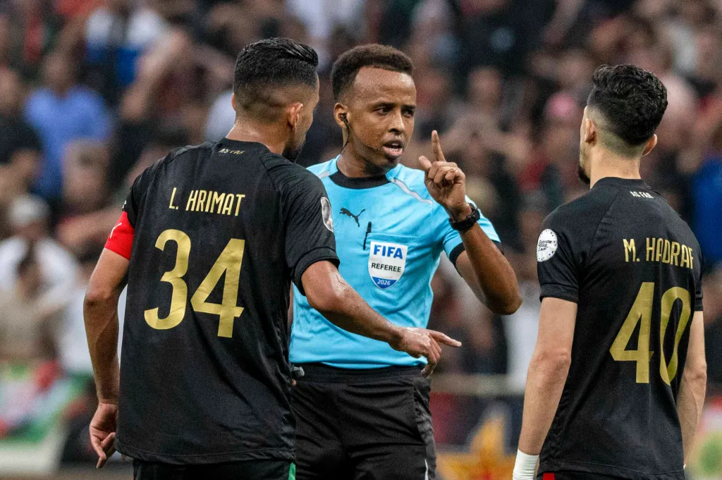 Referee Omar Artan confronts players L. Hrimat and M. Hadraf during a CAF Champions League final.