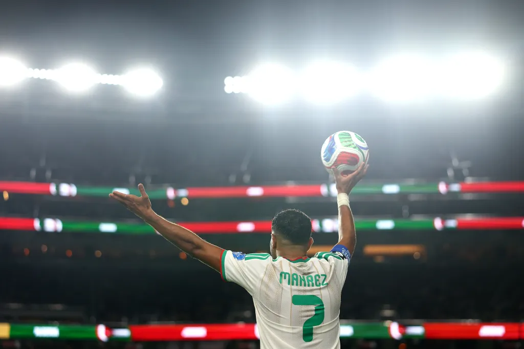 Riyad Mahrez of Algeria holding a soccer ball above his head, preparing for a throw-in during a FIFA World Cup 2026 match.