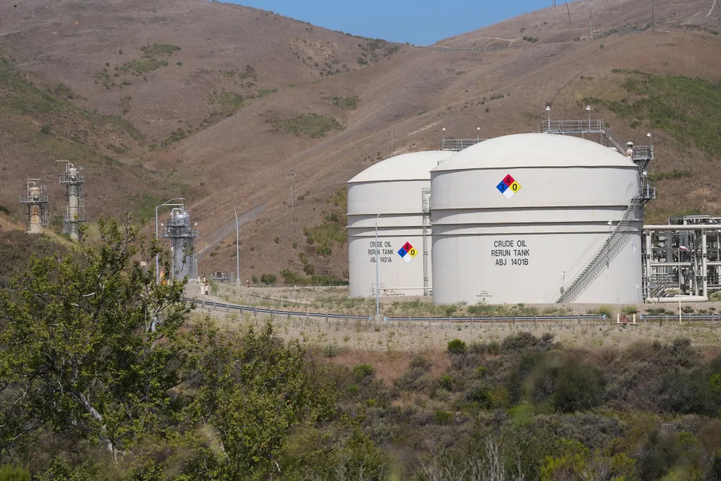 Oil and gas facility near Santa Barbara with two large "Crude Oil Rerun Tank" storage tanks and distant processing towers set against dry, scrubby hills.