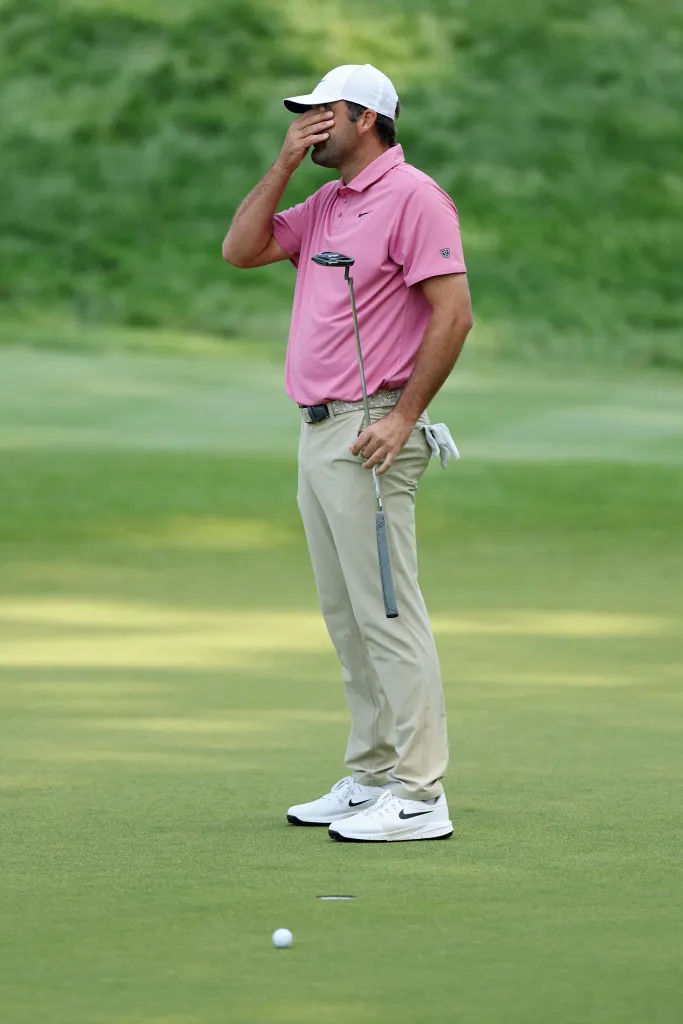 Golfer Scottie Scheffler reacts with his hand covering his face after missing a putt on the 18th green.