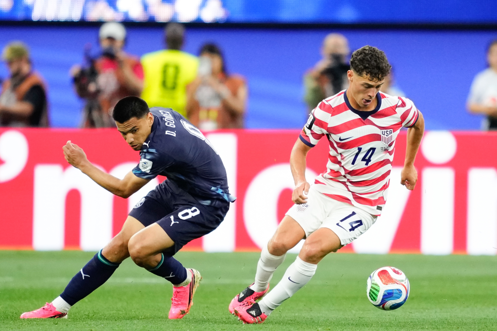 Sebastian Berhalter of USA and Diego Gomez of Paraguay compete for the ball during a soccer match.