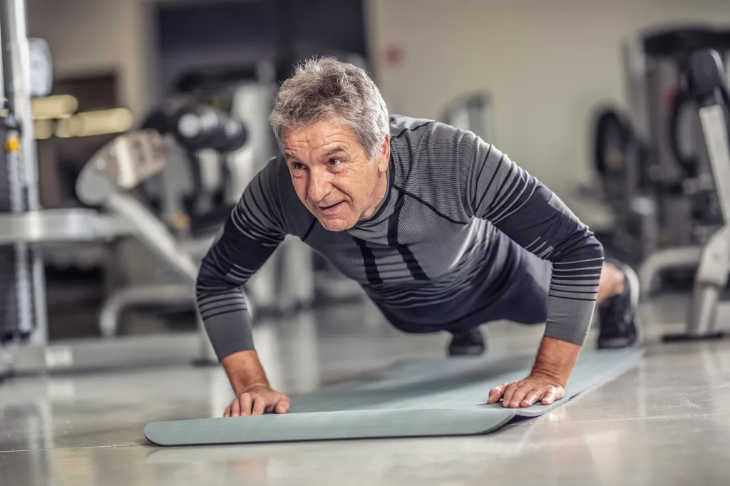 Senior man in sportswear doing pushups on a mat at the gym.