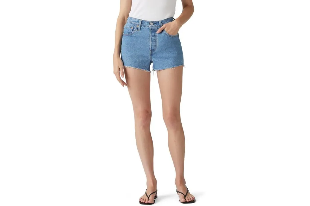 Light wash denim shorts with frayed hems worn by a person in a white top and black sandals.
