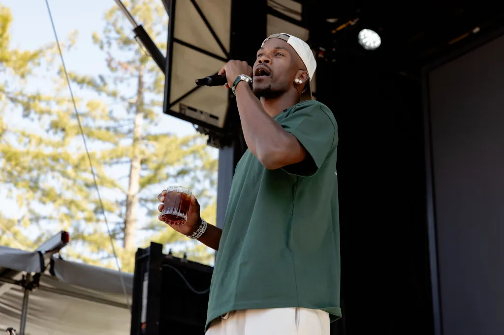 A man on stage holding a drink in one hand and a microphone in the other.