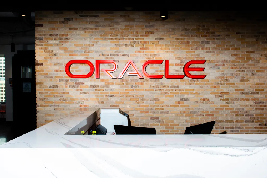The Oracle logo in red lettering above a front desk at an Oracle Cloud Infrastructure office.