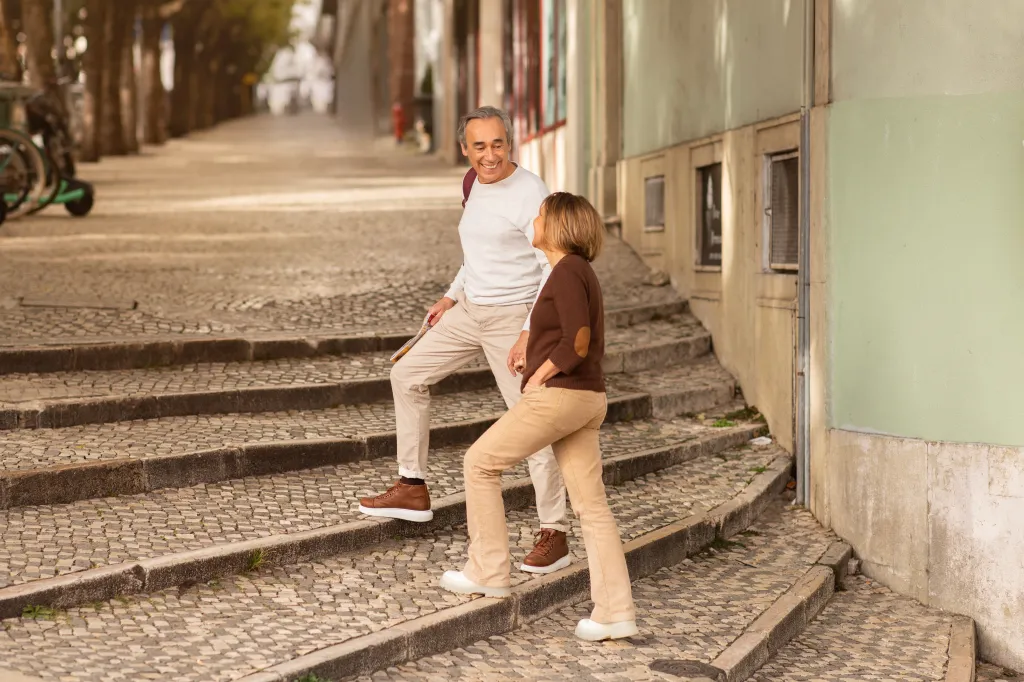 A cheerful mature couple walking hand-in-hand up a cobblestone street in Lisbon.