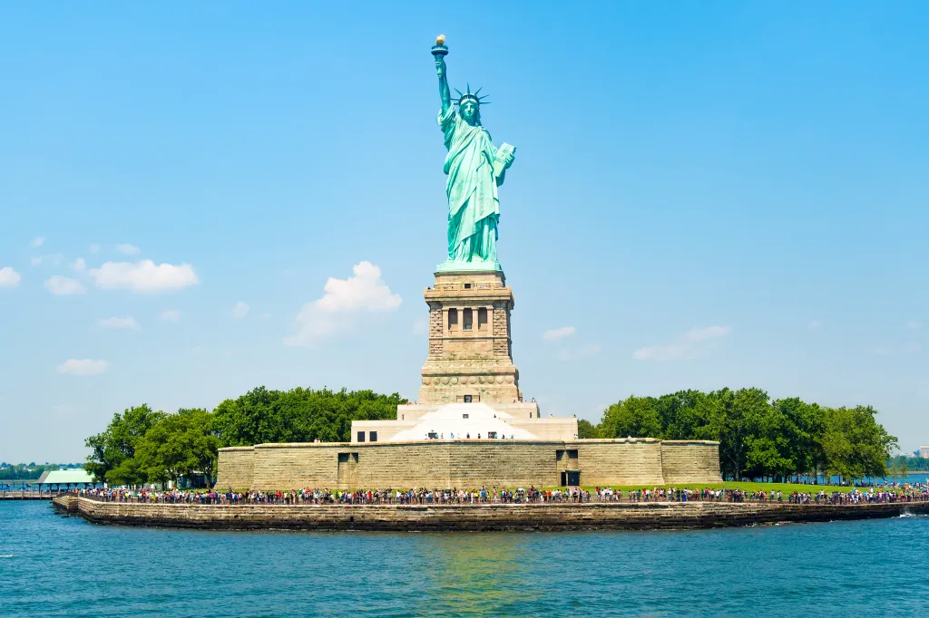 The Statue of Liberty on Liberty Island, with a line of visitors on the island's perimeter.