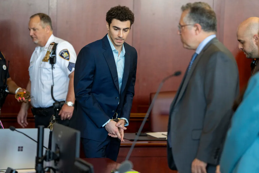 Luigi Mangione, accused of killing UnitedHealthcare CEO Brian Thompson, stands handcuffed in a courtroom.