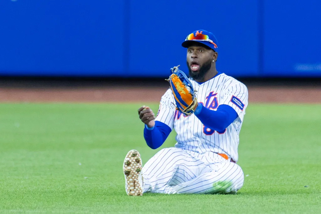 New York Mets center fielder Luis Robert Jr. sits on the ground with a look of surprise, having failed to catch a hit.