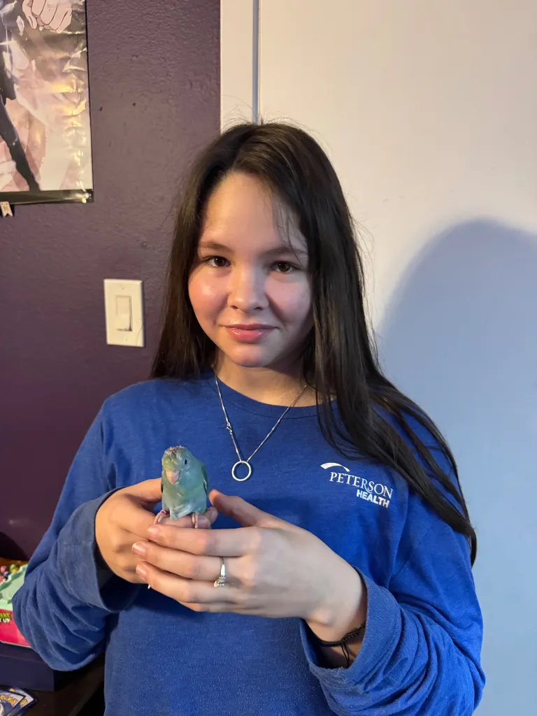 Kaydin Ruiz holding a light blue parakeet in her hands.
