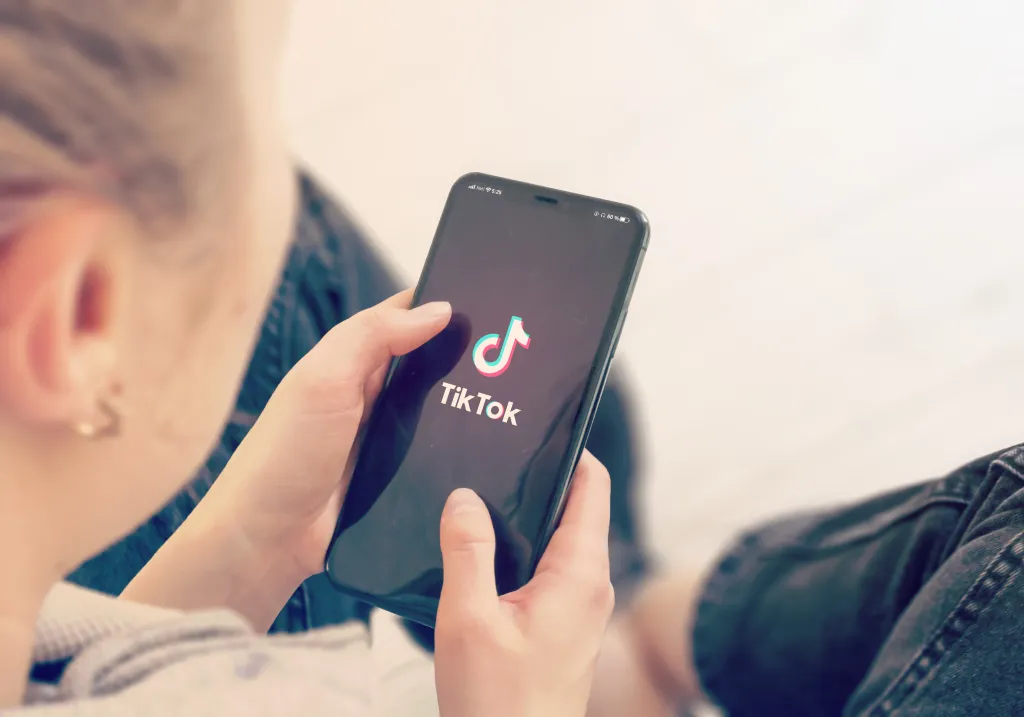 A young woman holding a smartphone displaying the TikTok logo.