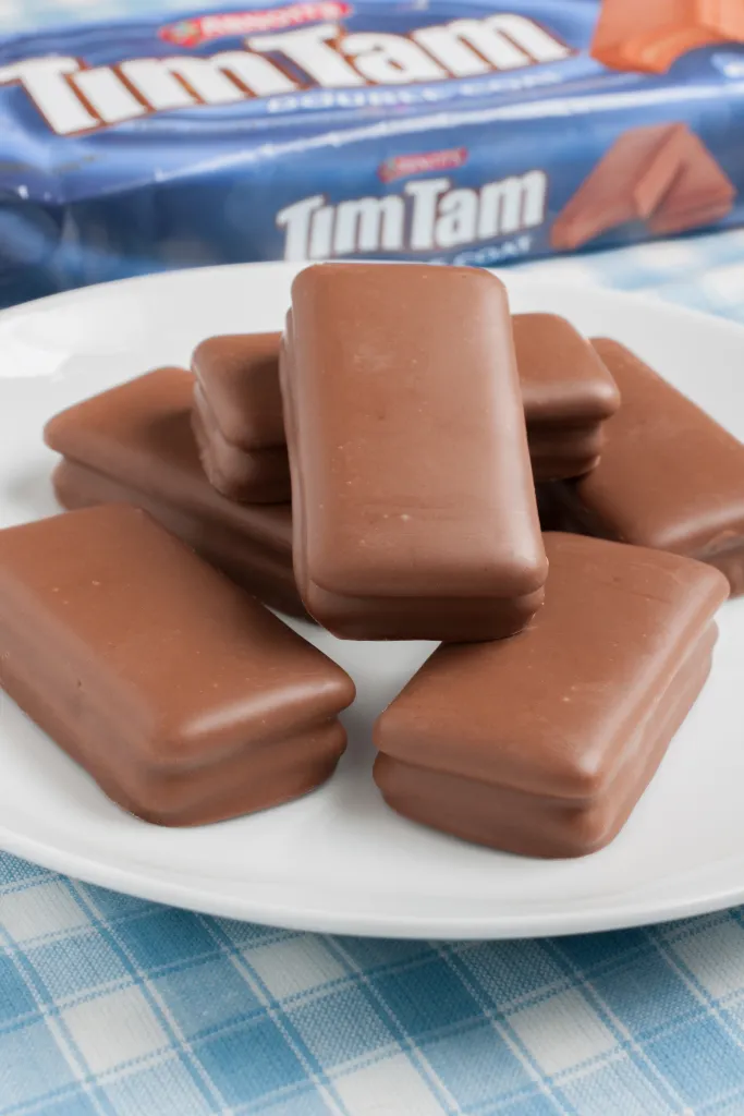 Tim Tam chocolate covered biscuits on a white plate with packaging in background.