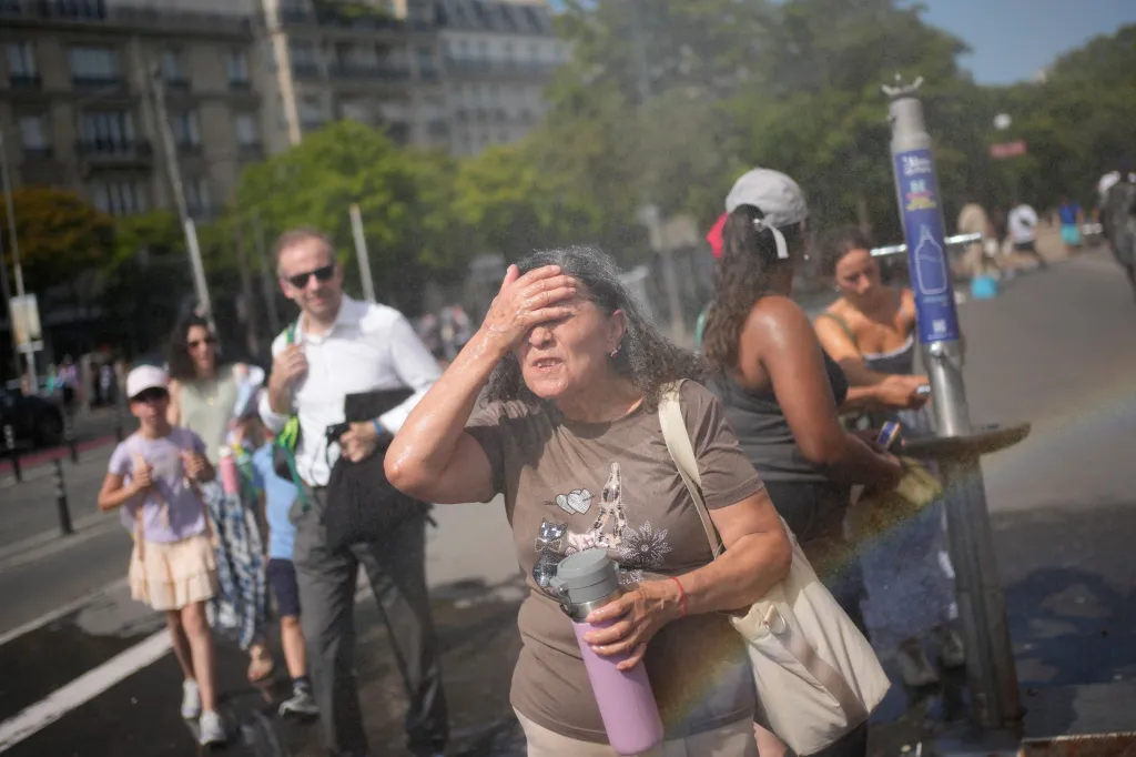 A woman shields her face from a public water fountain while others cool off in the background.