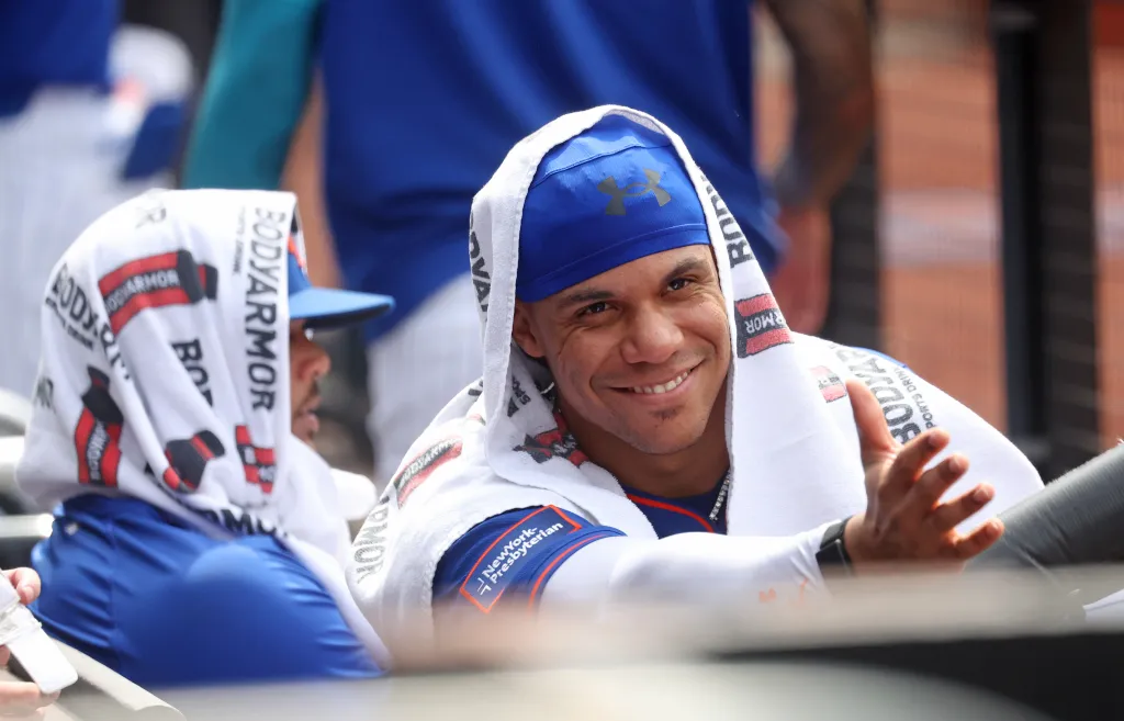 New York Mets left fielder Juan Soto smiles with a towel over his head in the dugout.