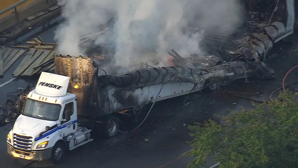 Two tractor-trailers crashed and caught fire on the New Jersey Turnpike, with one truck carrying lumber visible on the road.