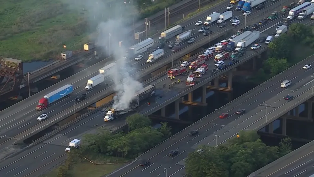 Aerial view of two tractor-trailers burning on a multi-lane highway, causing traffic to back up.