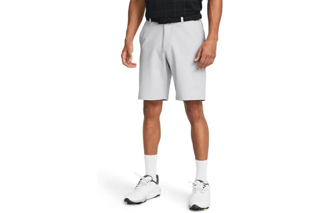 A man wearing light gray golf shorts, a black polo shirt, and white golf shoes.