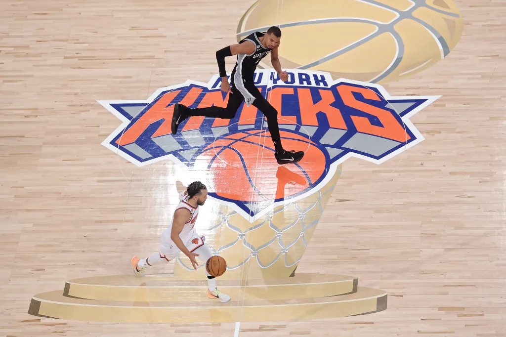 Jalen Brunson dribbles the basketball while Victor Wembanyama steps over the basketball hoop.