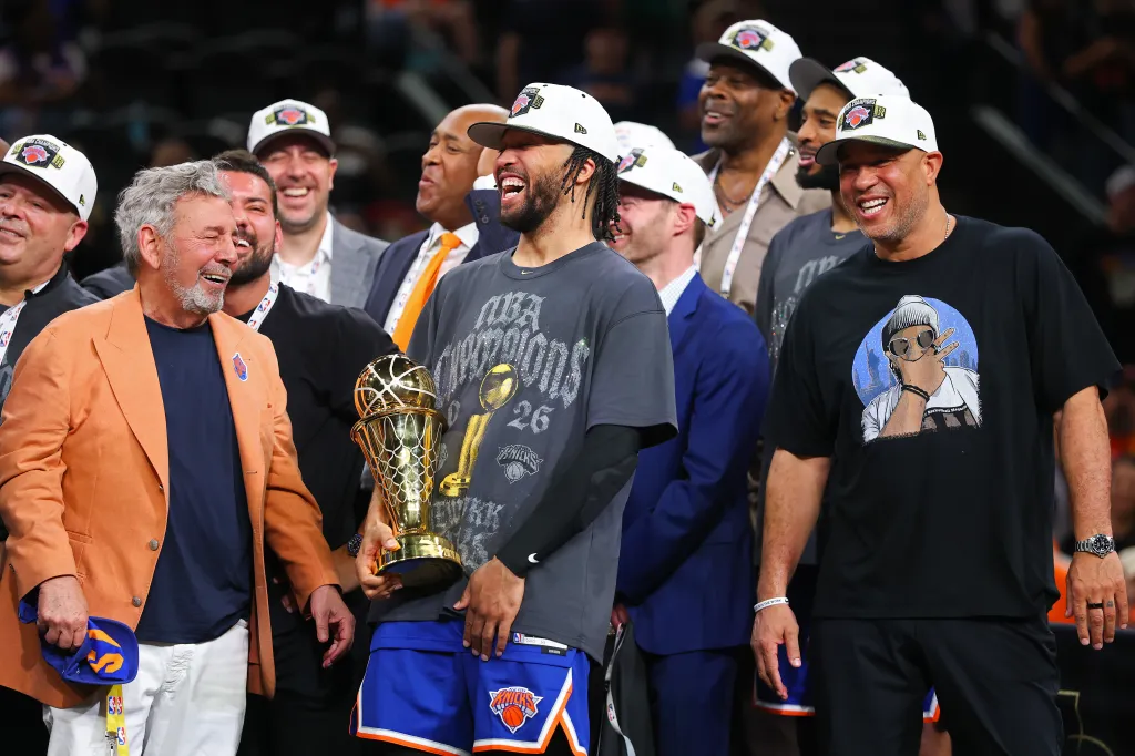 Jalen Brunson holds the NBA Finals MVP trophy, flanked by New York Knicks owner James Dolan and his father, Rick Brunson.