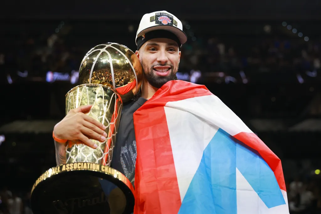Jose Alvarado holding the Larry O'Brien Championship Trophy with a flag over his shoulders.