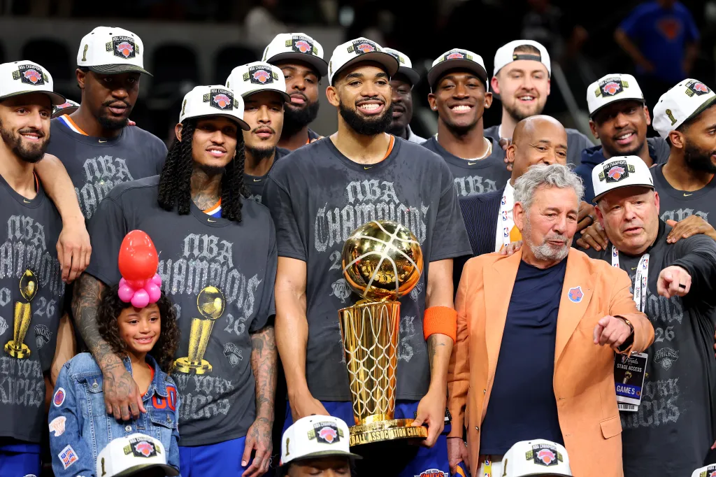Knicks center Karl-Anthony Towns #32 celebrates with the Larry O'Brien Championship trophy and owner James Dolan in an orange blazer after the victory against the San Antonio Spurs in Game 5 of the 2026 NBA Finals at Frost Bank Center on June 13, 2026 in San Antonio, Texas.