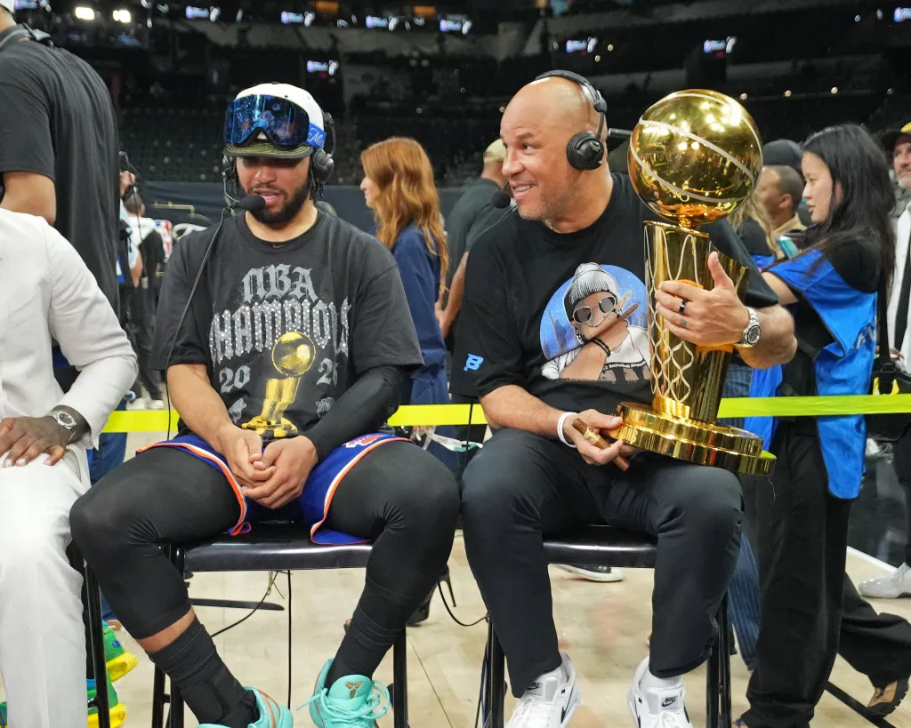 Jalen Brunson and Rick Brunson smiling with the Larry O'Brien Championship Trophy.