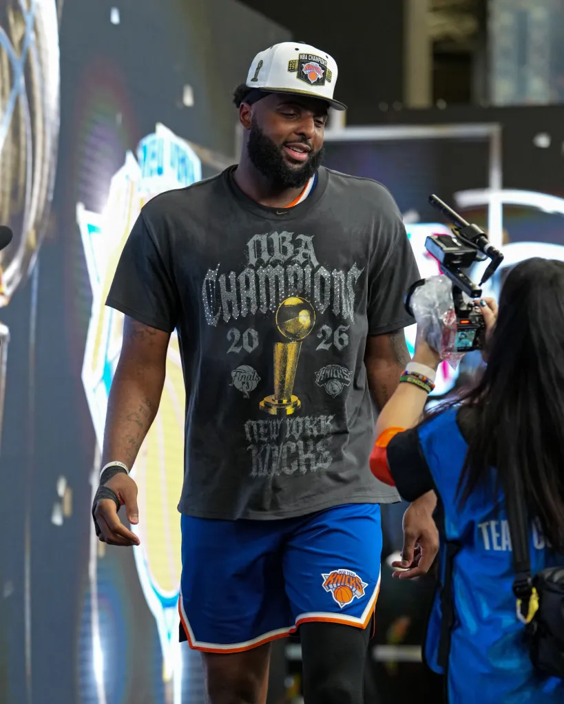 Mitchell Robinson smiling while wearing an NBA Finals Champions hat and a T-shirt that reads "NBA Champions 2026 New York Knicks."