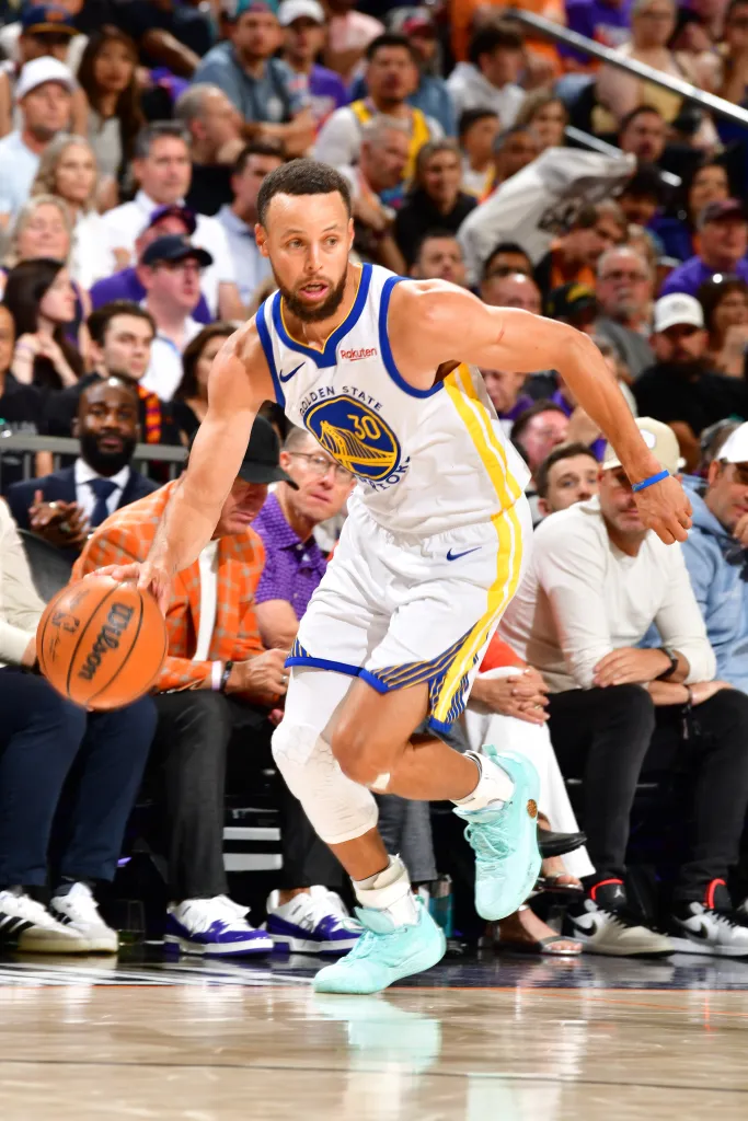 Stephen Curry dribbles the basketball while wearing a white Golden State Warriors uniform.