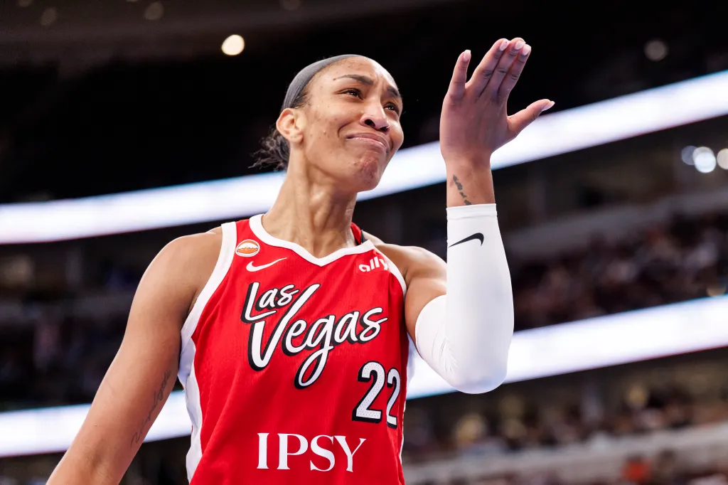 A'ja Wilson in a red Las Vegas Aces jersey, raising her right hand.