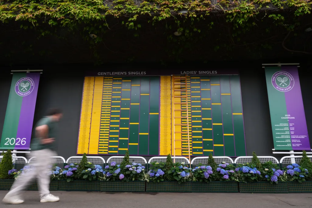 A visitor walks by the Gentlemen's Singles and Ladies' Singles match boards at Wimbledon.