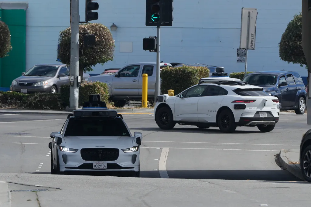 Two white Waymo self-driving cars on a city street.