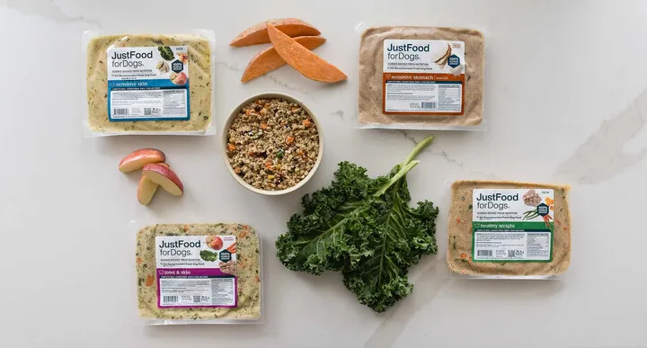 Variety of JustFoodForDogs packaged dog food with fresh ingredients like apples, sweet potatoes, and kale.