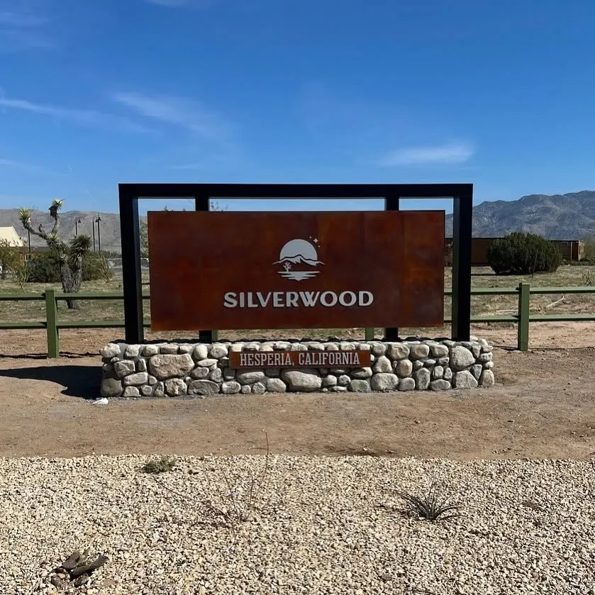 A sign for Silverwood, Hesperia, California, with a mountain and sun logo, set against a desert landscape.
