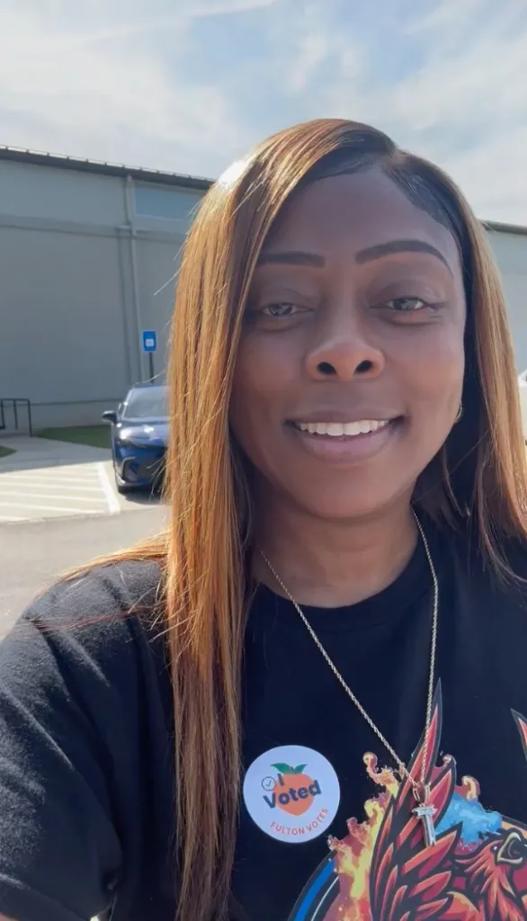 Tiffany Henyard smiling after voting, with an "I Voted Fulton Votes" sticker on her shirt.