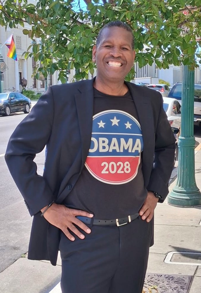A man wearing a black suit and a black t-shirt with an "Obama 2028" logo.