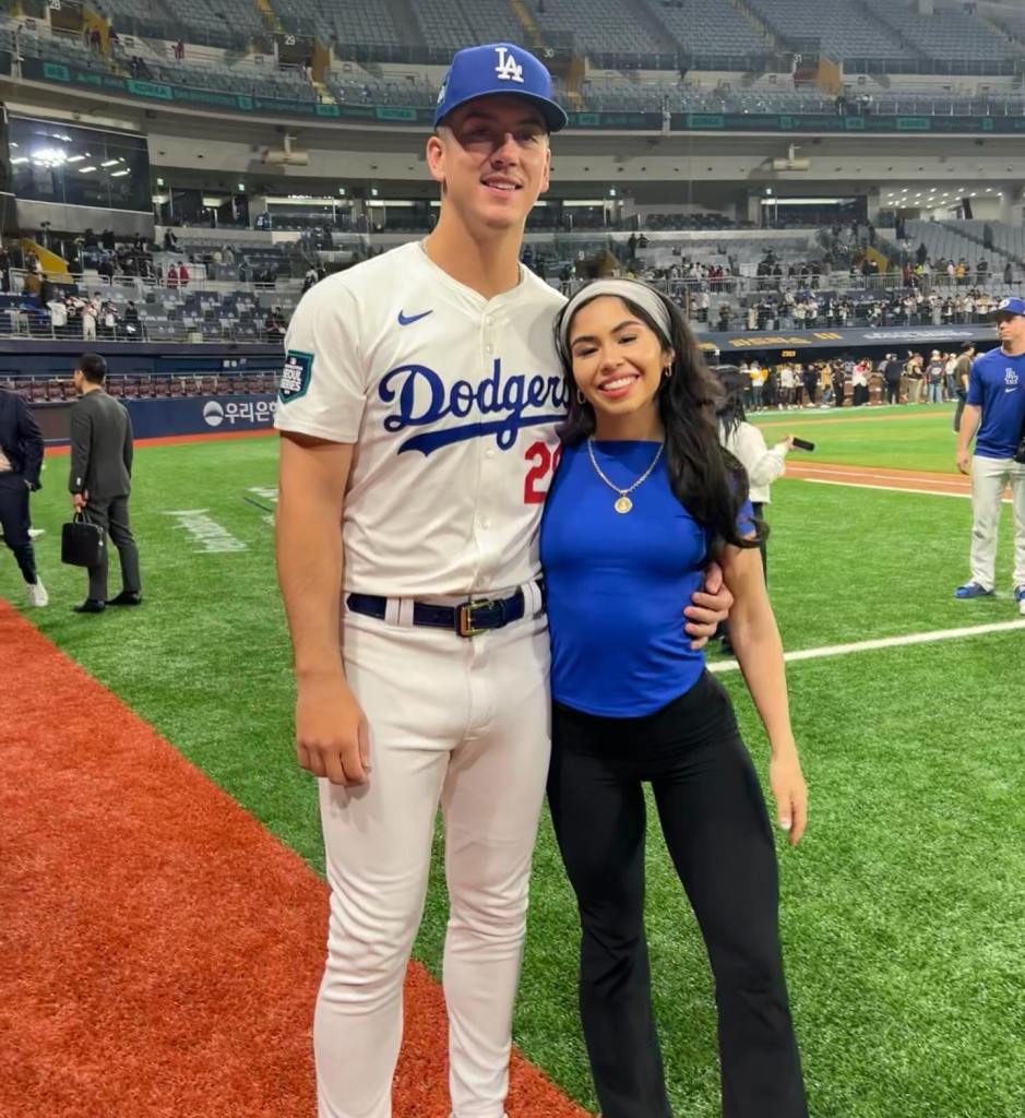 Bobby Miller, wearing a Dodgers uniform, and Natalie Loureda, in a blue shirt, smiling on a baseball field.